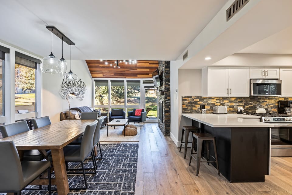 Airy great-room layout connecting the dining space, kitchen, and living area. Enjoy meals at the large table, gather at the island barstools, and flow seamlessly into the cozy lounge beyond.