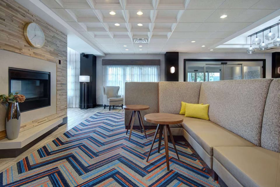 Lobby with fireplace, bright windows, and colorful carpet seating
