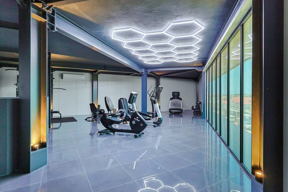 Modern fitness center at Aruba Racquet Club featuring polished grey tile, floor-to-ceiling windows, cardio machines, and a honeycomb LED ceiling light.