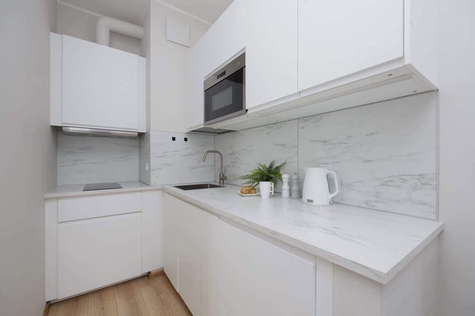 A narrow kitchen section with upper cabinets and a built-in hood. The cooking area appears neatly organized and well-lit. Neutral colors dominate the design.