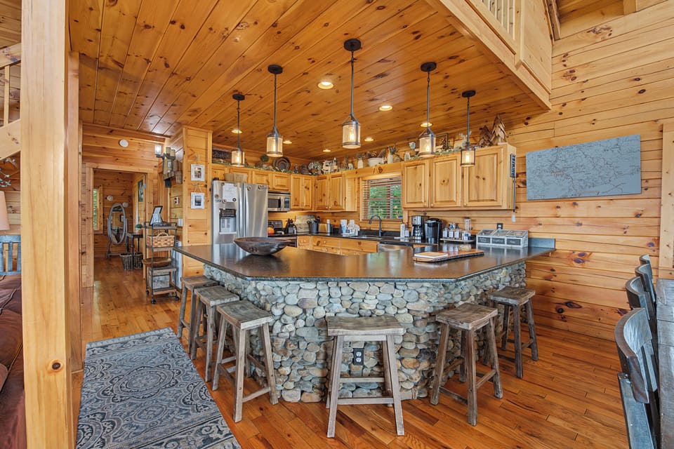 Your rustic mountain retreat features a stunning stone-clad island with bar seating, premium appliances, and warm wood finishes that create the perfect gathering spot for memorable meals together.