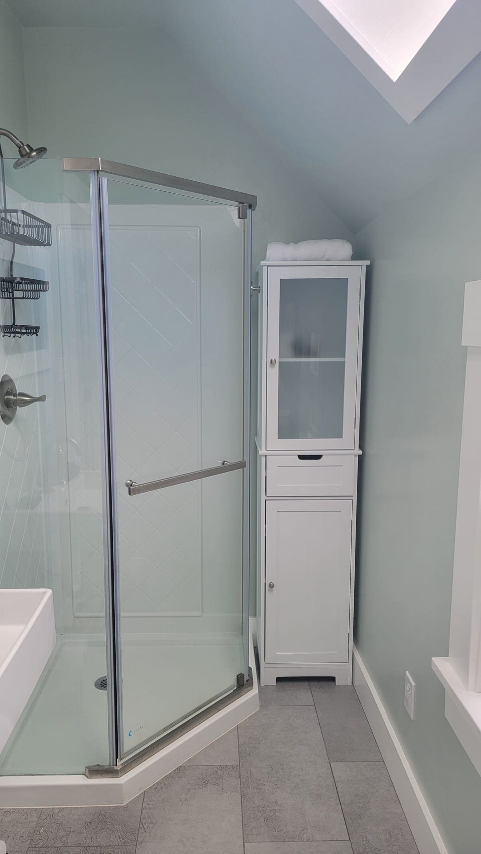 Modern bathroom with sink, shower, toilet, and storage. Skylight and window.