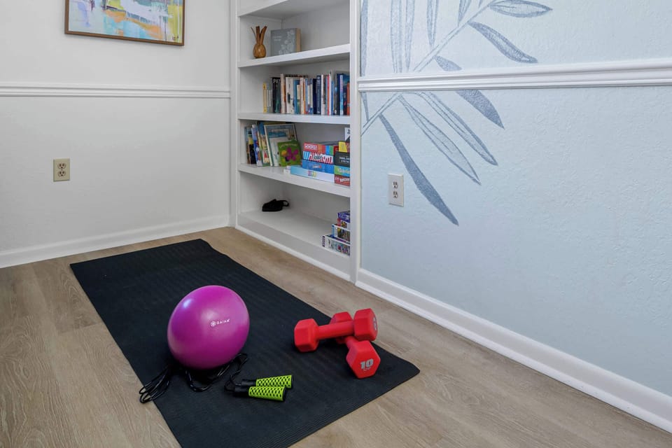 A tucked-away workout nook keeps a yoga mat, ball, and dumbbells handy beside the bookshelf. - Home Gym Nook - The Hammock - Largo, FL