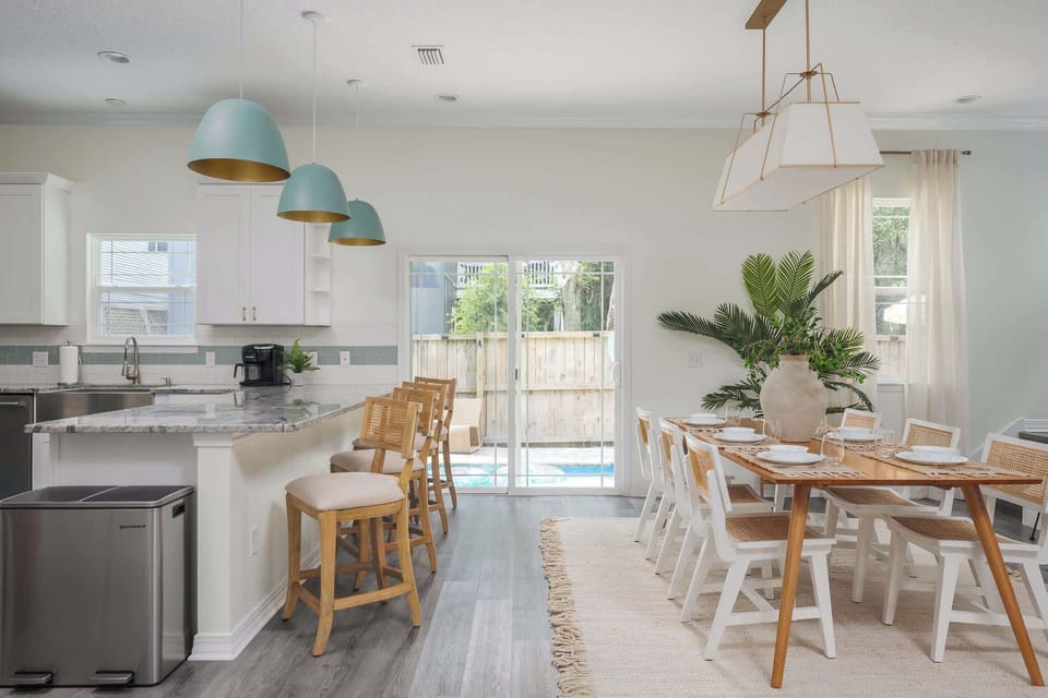 "Cook together in a bright, open kitchen with granite counters, sea‑glass lights, rattan stools and a farmhouse table. Slide open the doors and let the poolside breeze in for family dinners or happy hours. - The Coquina - St. Augustine, FL"