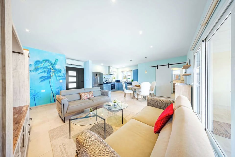 Relax in this airy space with a palm tree mural, comfy sofas, and easy access to the kitchen and dining area. Slide open the glass doors to enjoy indoor-outdoor living.