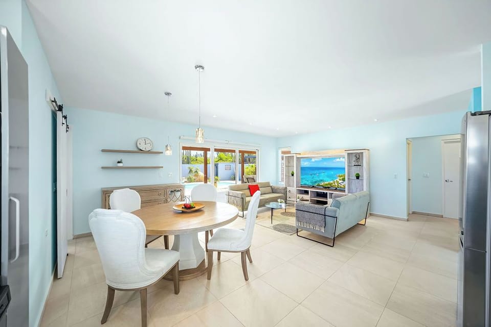 Welcome to the heart of the home—an open-concept space with a stylish dining area, cozy living room, and soft blue walls. Enjoy meals, relax on plush sofas, and peek through sliding doors to your private outdoor oasis.