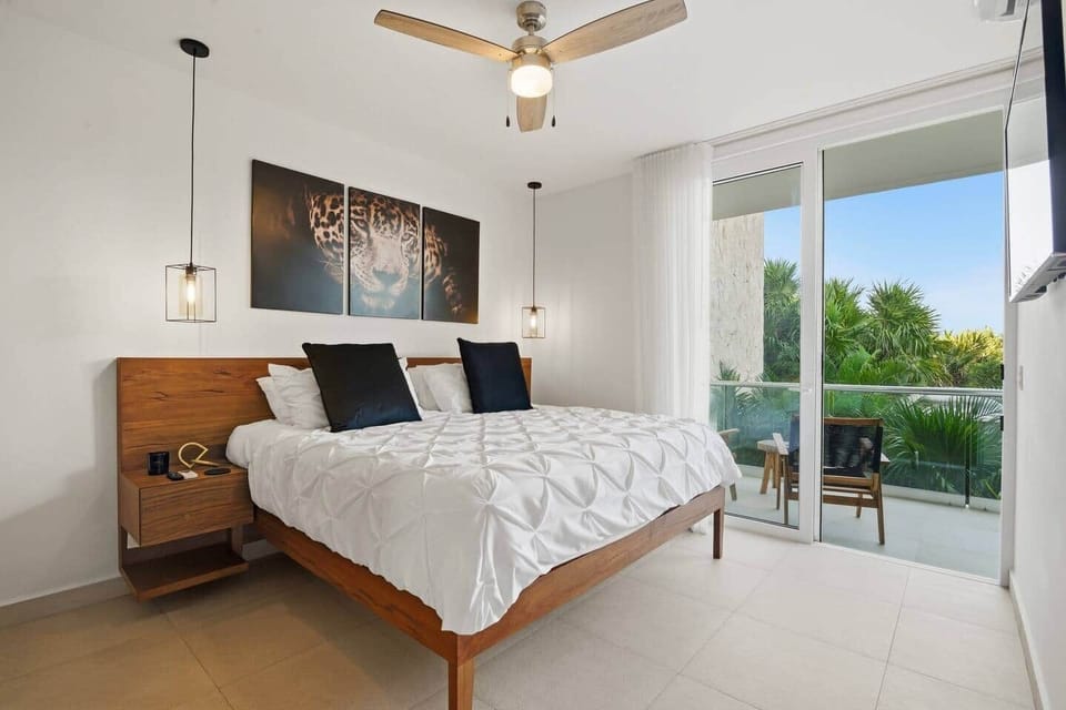 Relax in this inviting bedroom featuring a plush king bed, TV, AC, ceiling fan, ample wardrobe, and room-darkening shades for a restful sleep. Sliding glass doors lead to a private balcony with beautiful greenery and pool views.
