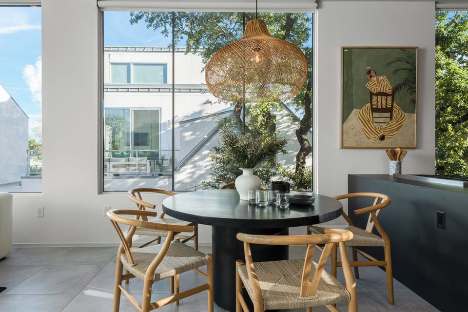 Dining area with a round wooden table, woven chairs, and a large hanging light fixture.