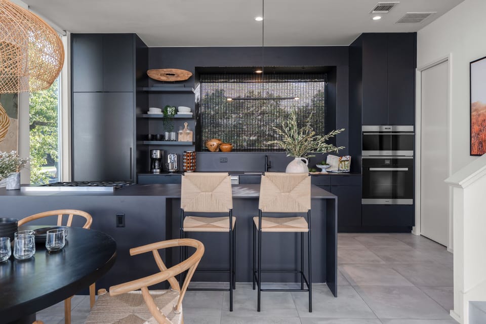 Contemporary black kitchen with island, wooden bar stools, and dark cabinetry.