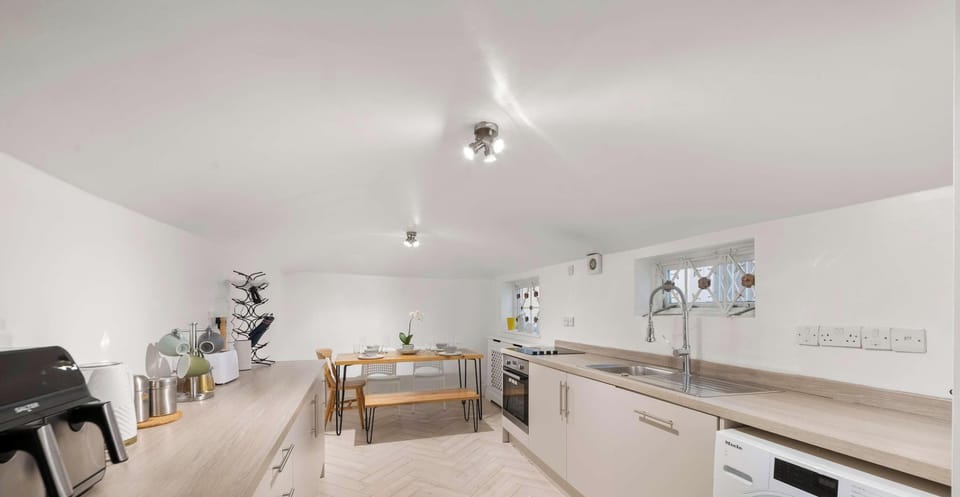 Modern galley kitchen featuring light wood counters, white cabinets, and herringbone flooring. A simple wooden dining set is tucked into the far end.
