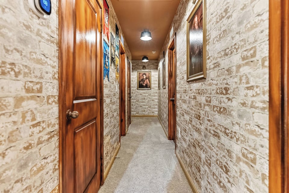 Step into a charming hallway adorned with textured stone walls that evoke warmth and character, complemented by rich wooden doors. Soft, ambient lighting illuminates the space, creating an inviting transition to the rooms beyond.