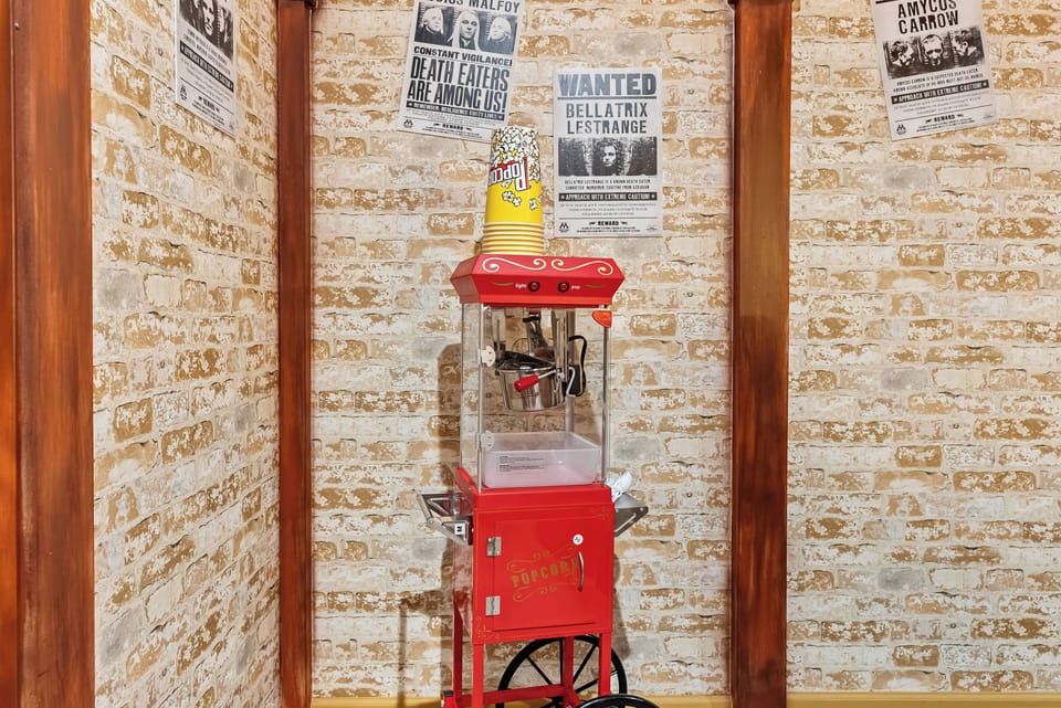 Immerse yourself in a playful atmosphere featuring a vintage popcorn machine with a vibrant red hue against rustic wallpaper adorned with Western-themed posters, creating a cozy spot for movie nights or snack breaks.