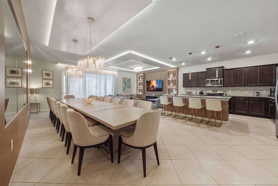 Enjoy our spacious dining area with a sleek wooden table and plush cream chairs, all illuminated by soft recessed lighting and a stylish chandelier, creating a warm ambiance ideal for your gatherings.