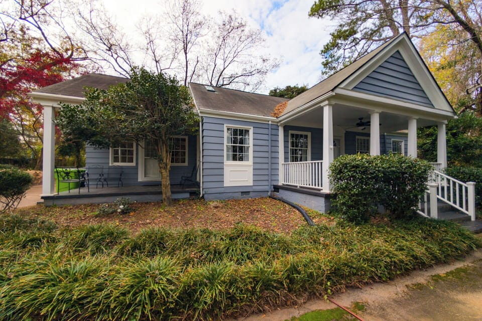 The exterior of this lovely home boasts soft blue siding and a crisp white railing. A secondary covered porch area provides extra outdoor seating, all nestled behind well maintained hedges and a beautiful landscape.