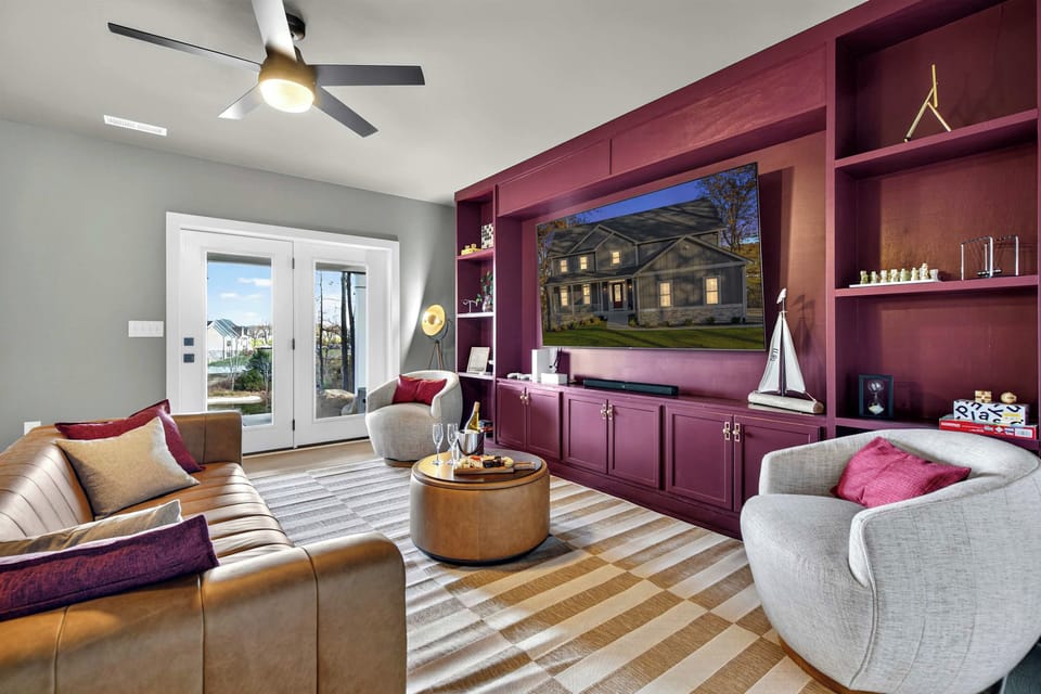 Lower Level Lounge - A bold plum entertainment wall with a big-screen TV, leather sofa, and swivel chairs creates a second living space with patio access.