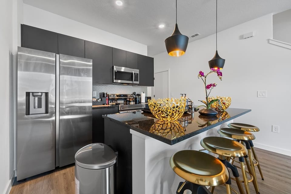 Modern kitchen with stainless steel appliances and a black granite island featuring gold-accented bar stools.