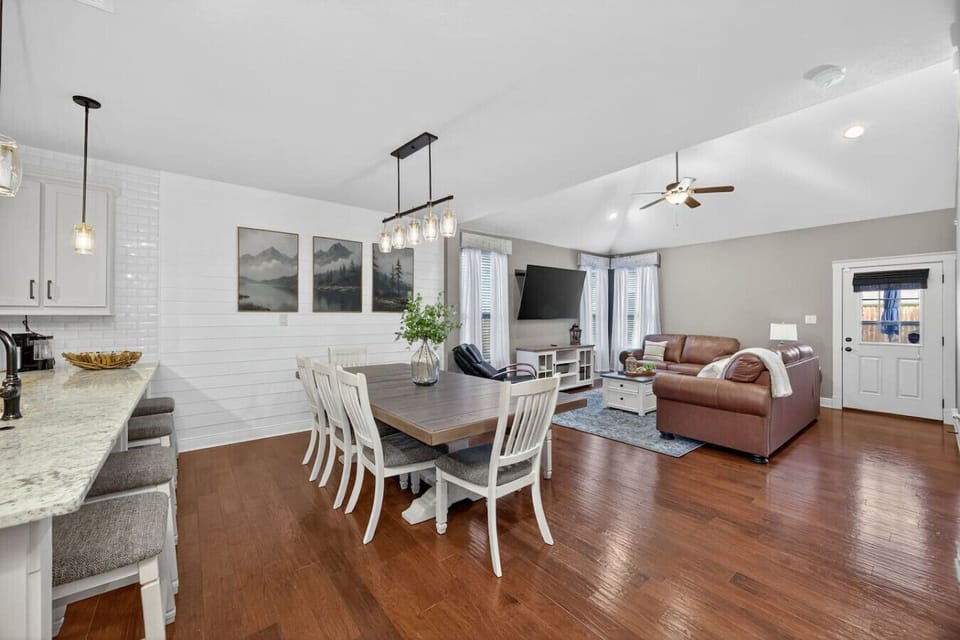 Spacious open-concept layout with a large dining table, cozy leather seating, and bright natural light. Perfect for family meals, movie nights, and relaxing together in comfort.