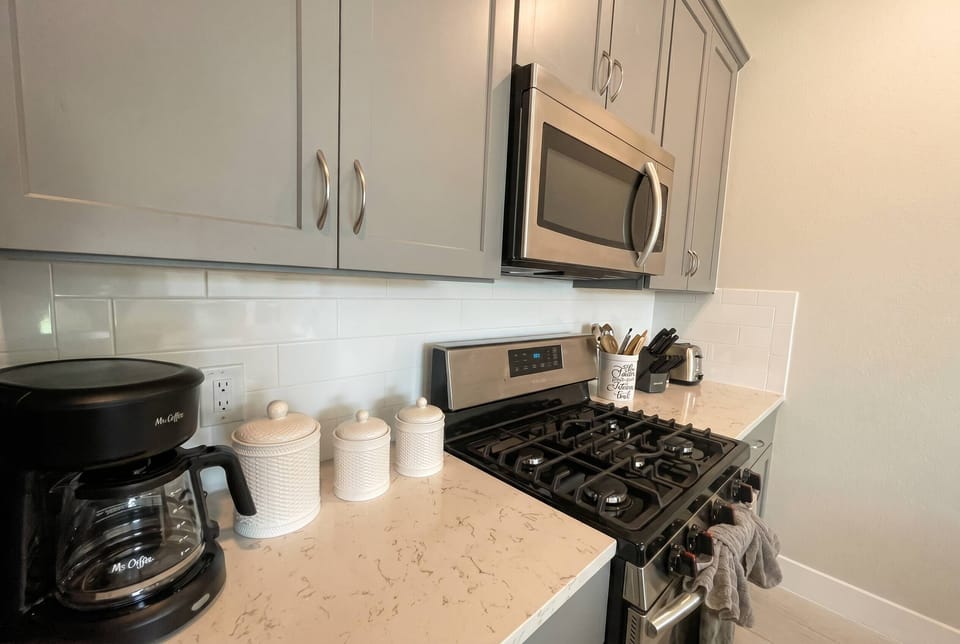 This inviting kitchen boasts sleek gray cabinets and a bright white countertop, creating a functional space for meal prep. With stainless steel appliances and a stylish coffee maker, you'll enjoy starting your day in comfort.
