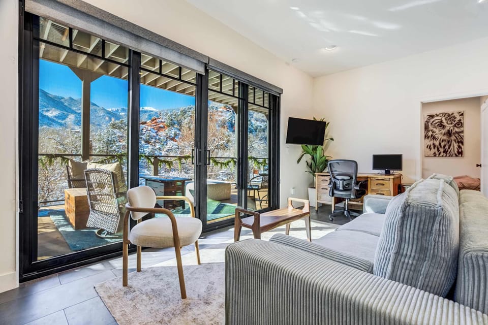 Floor-to-ceiling glass brings the mountains right into the living room, where modern seating, a dedicated desk setup, and easy access to the balcony make the space feel open and effortless.