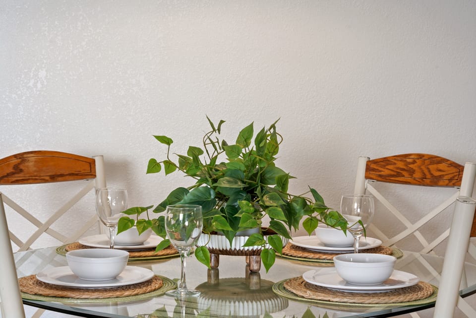 Close‑up of the dining table with white dishes, wine glasses, and lush plant centerpiece.