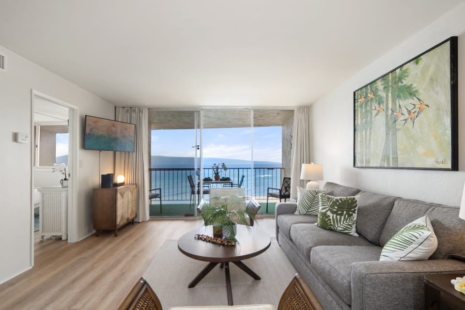 Living room with sofa, coffee table, and wall art, opening to the balcony through wide glass doors.