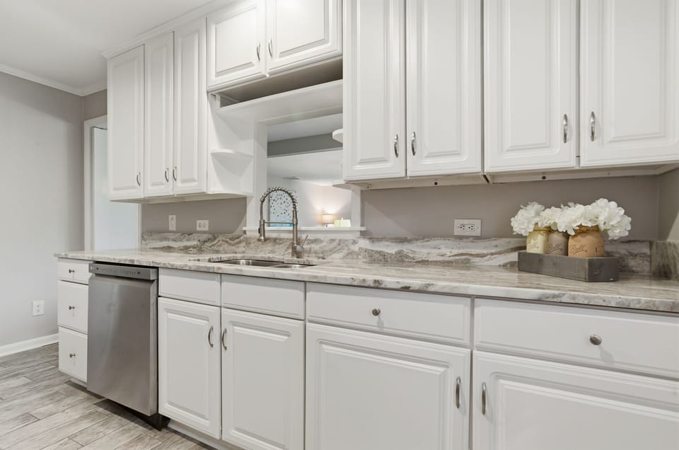 Your pristine white kitchen sparkles with granite countertops and modern appliances, ready for morning coffee or evening meals.