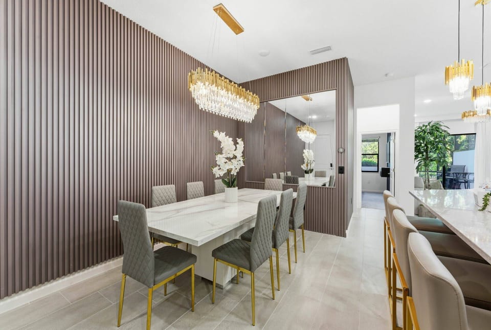 Brighten your dining experience in a chic space featuring a sleek glass table surrounded by plush gray chairs. The striking wood-paneled wall and elegant chandelier create a sophisticated atmosphere, perfect for gatherings.