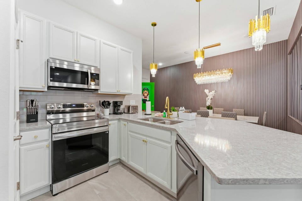 This inviting kitchen features bright white cabinetry and stainless steel appliances, with elegant pendant lighting adding warmth. The spacious counter is perfect for meal prep or casual dining, enhancing your culinary experience.