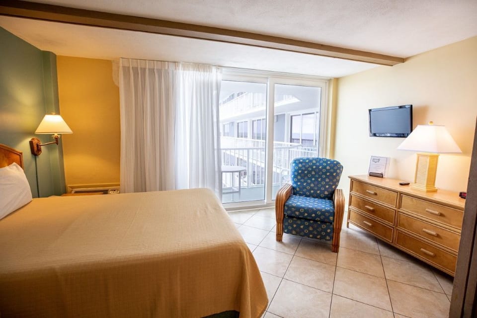 Bright sunlight floods the bedroom, creating a warm and relaxing atmosphere, complete with a balcony for ocean views.