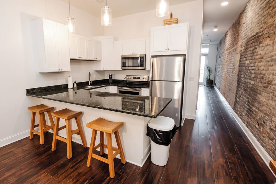 Open kitchen with eat-in bar and exposed-brick hallway leading to the balcony