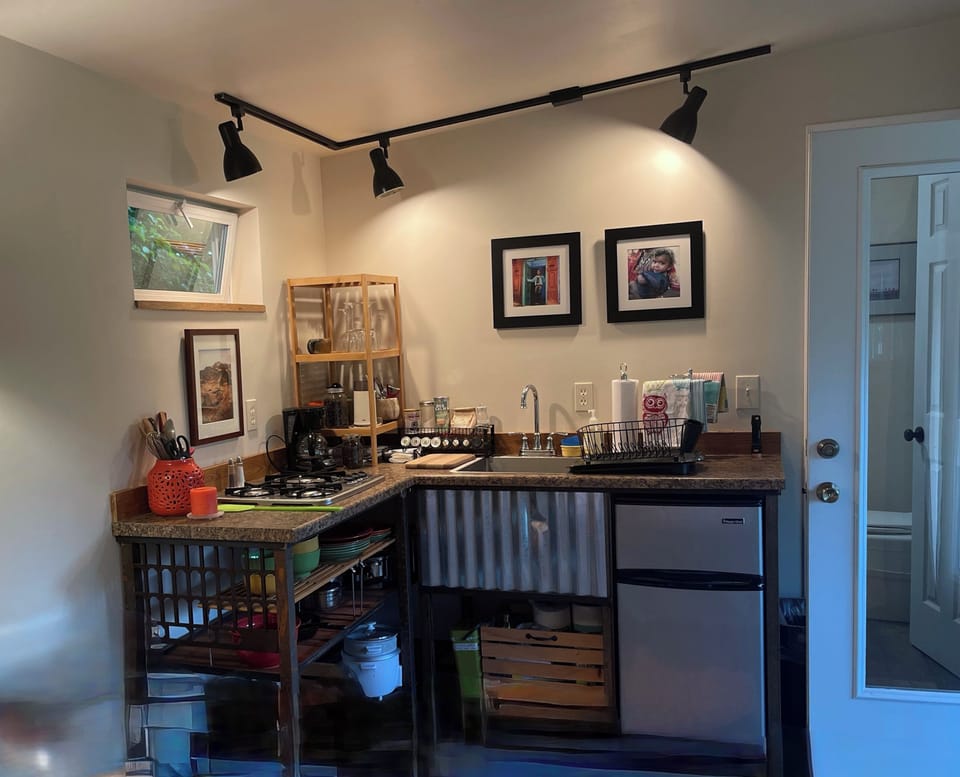 Kitchenette with small refrigerator, stove top, microwave, sink, and dishes.