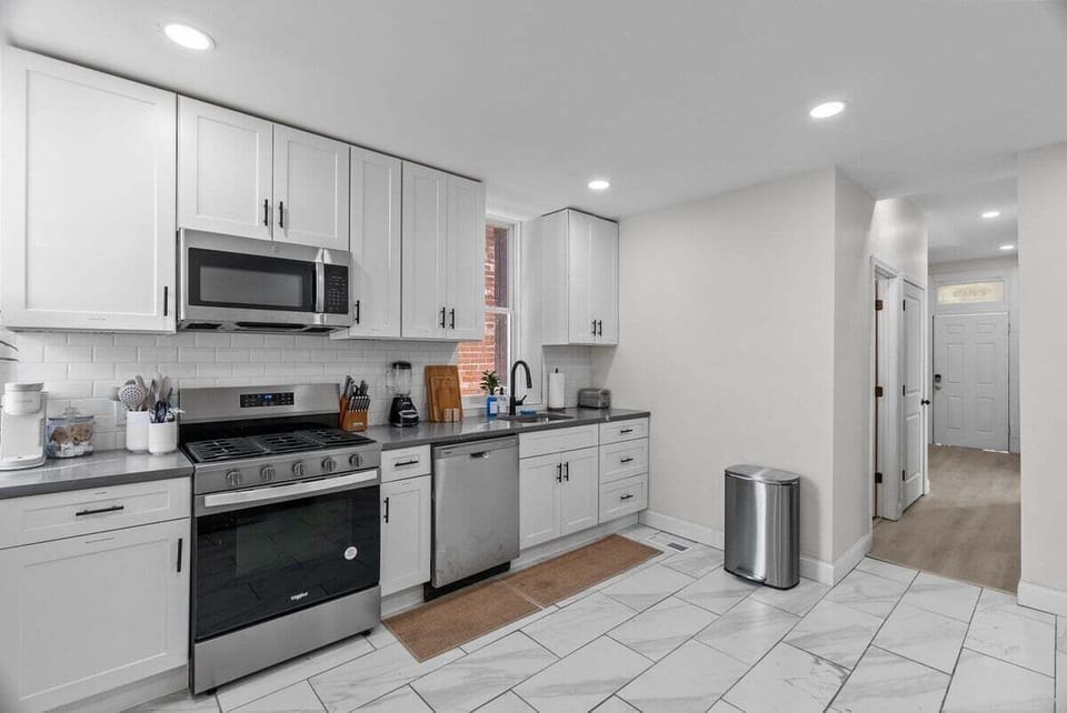 The opposite kitchen angle shows the range, dishwasher, sink, cabinetry, and connection to the front hall.
