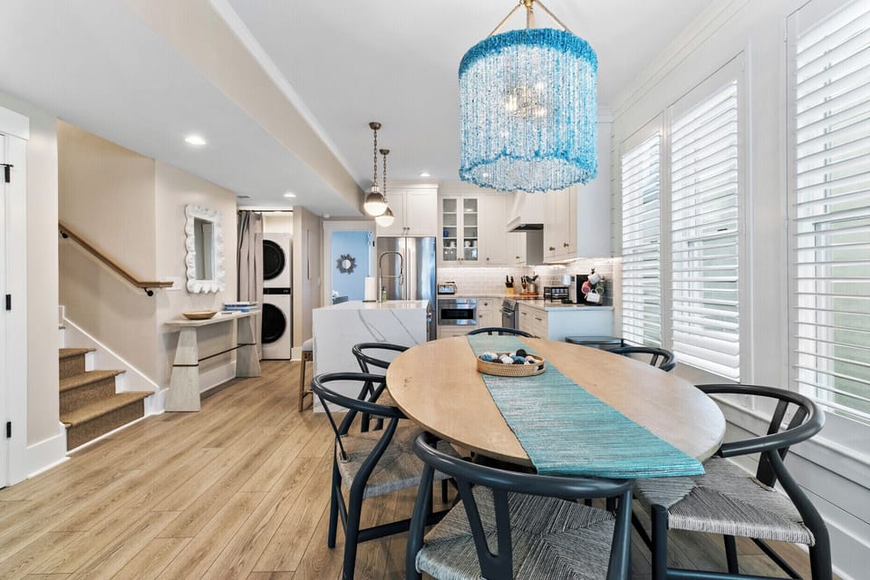 A light-filled space featuring a statement blue chandelier, natural wood tones, and relaxed seating—perfect for seaside-inspired gatherings.