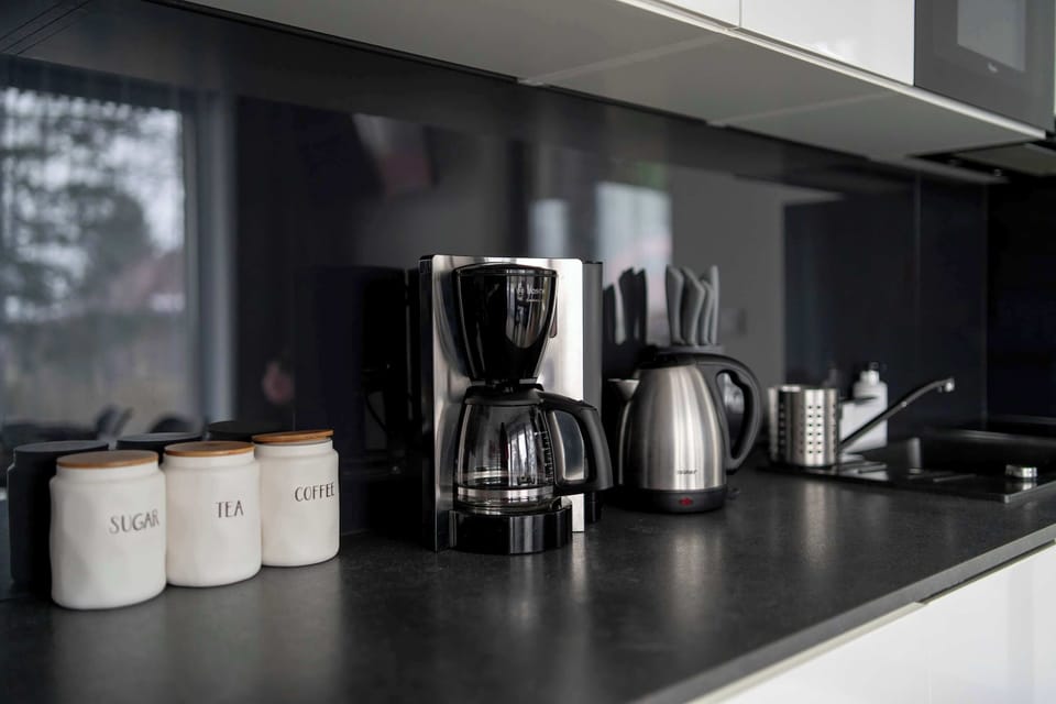The kitchenette includes a coffee corner with modern appliances. Dark finishes give the space a stylish, contemporary look.