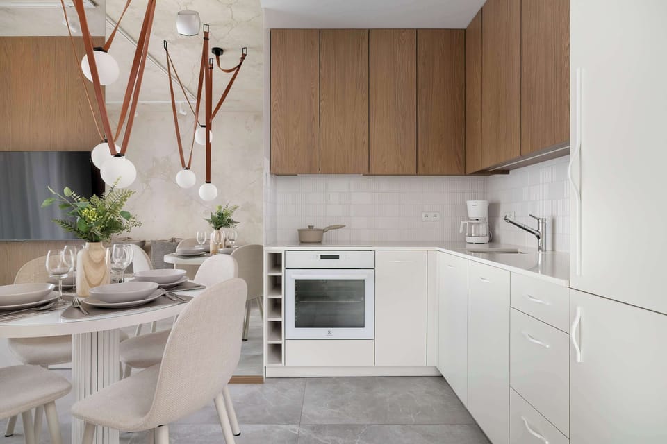 A modern kitchenette with white cabinetry and wooden upper units. It is fully equipped for everyday cooking and short stays