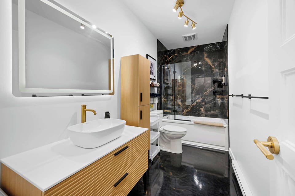Salle de bain élégante, inspirée d’un spa, avec une vanité moderne et une douche-baignoire luxueuse — conçue pour offrir un confort total aux invités.