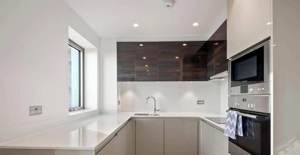 This modern U-shaped kitchen features a sleek, minimalist design with glossy white countertops and two-toned cabinetry. Dark wood accents and stainless steel appliances create a clean, sophisticated aesthetic.