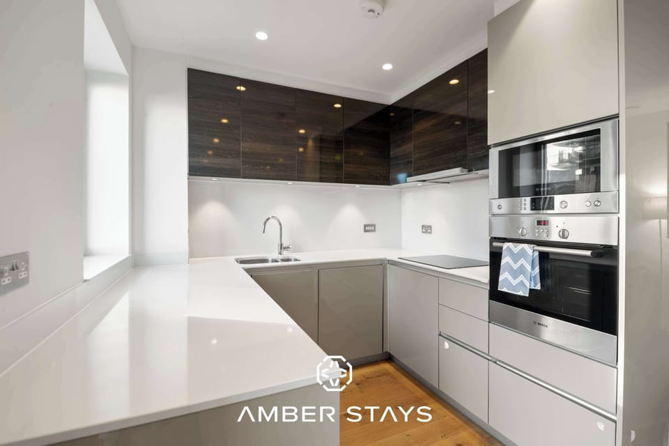 This modern U-shaped kitchen features a sleek, minimalist design with glossy white countertops and two-toned cabinetry. Dark wood accents and stainless steel appliances create a clean, sophisticated aesthetic.
