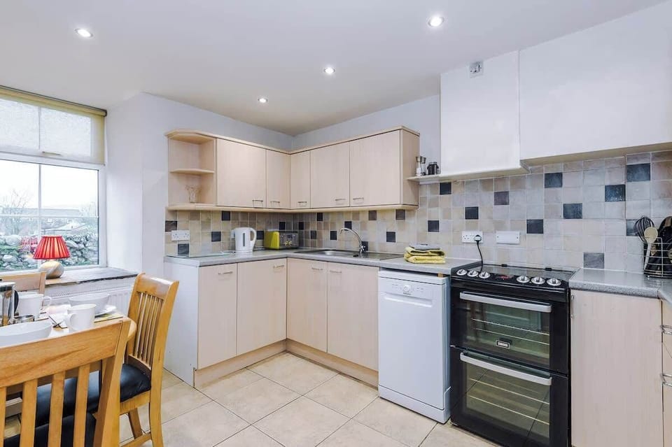 A bright, modern kitchen features light wood cabinetry and a mosaic tile backsplash, complete with a freestanding black oven and integrated appliances.