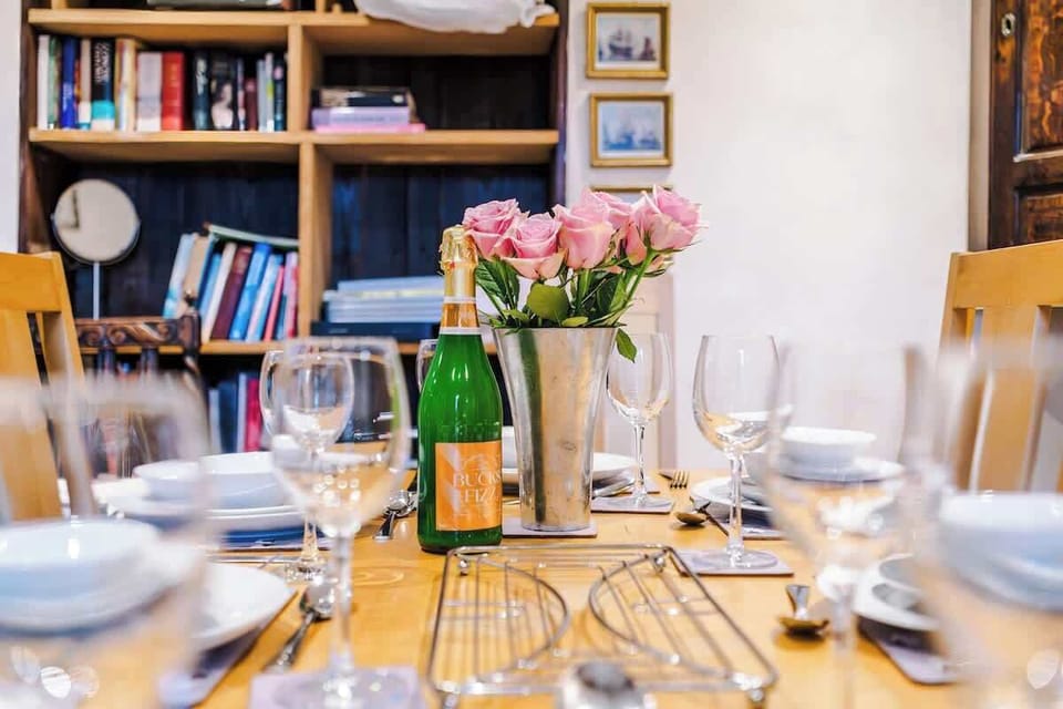 An elegant table setting features a chilled bottle of sparkling wine and a bouquet of pink roses, creating a welcoming atmosphere for a special meal.