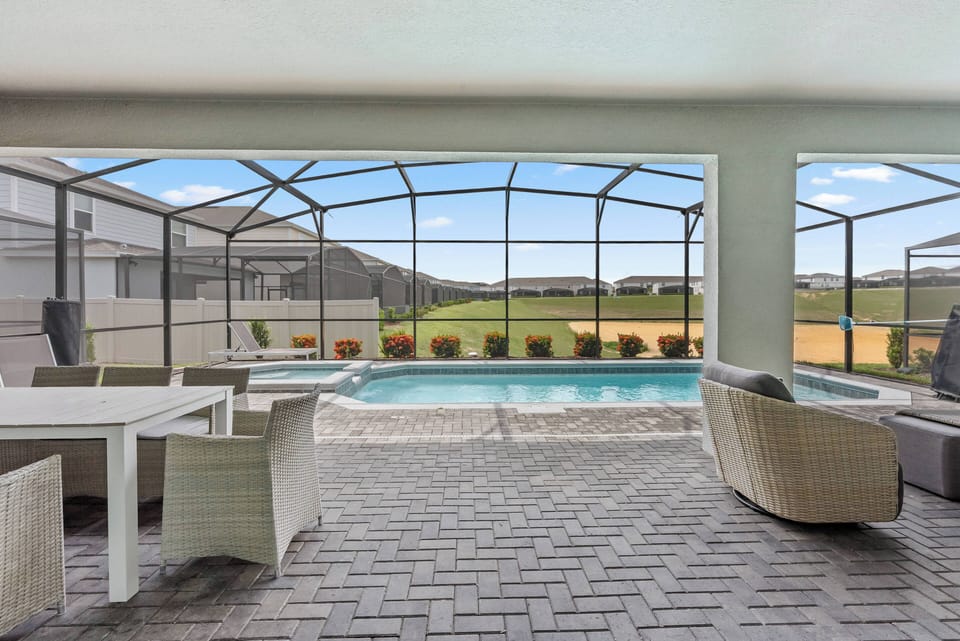 Step onto a spacious patio with stylish wicker furniture, ideal for lounging or dining. The screened enclosure provides an unobstructed view of the shimmering pool and lush landscape, inviting you to relax and soak up the sun.