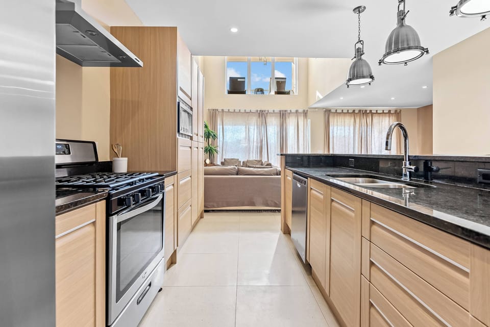 Welcome to a stylish kitchen with sleek black countertops and warm wooden cabinetry, creating a cozy atmosphere. Large windows fill the space with natural light, perfect for inspiring all your culinary adventures.