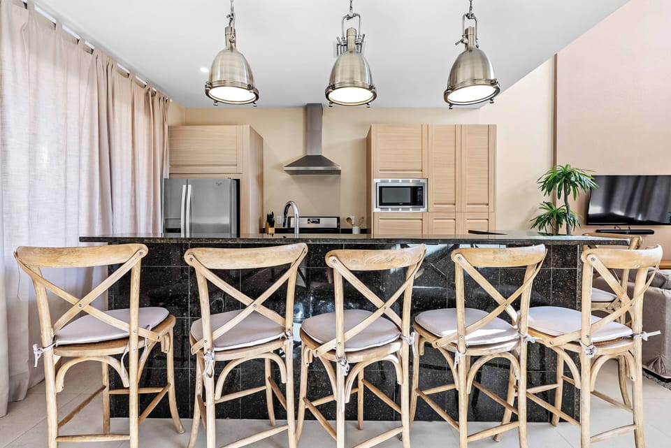 Bring your friends to the stylish black island with five cozy wooden stools, where modern pendant lights create a warm atmosphere in this spacious kitchen, complete with light wood cabinetry for all your culinary adventures.
