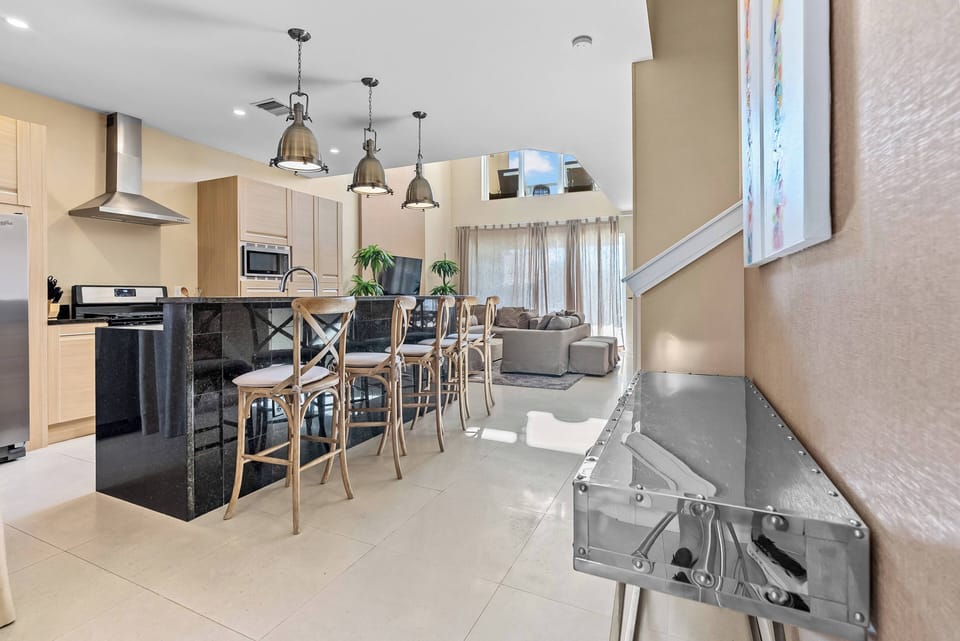 Step into an airy kitchen featuring sleek black countertops and warm wooden cabinetry, ideal for cooking your favorite meals. The stylish bar stools invite casual gatherings, while large windows fill the space with natural light.