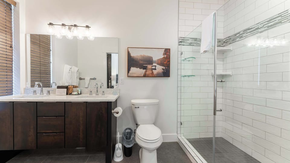 Start and end your day in this stylish bathroom featuring a contemporary vanity, bright lighting, and a glass-enclosed shower with clean, modern finishes.