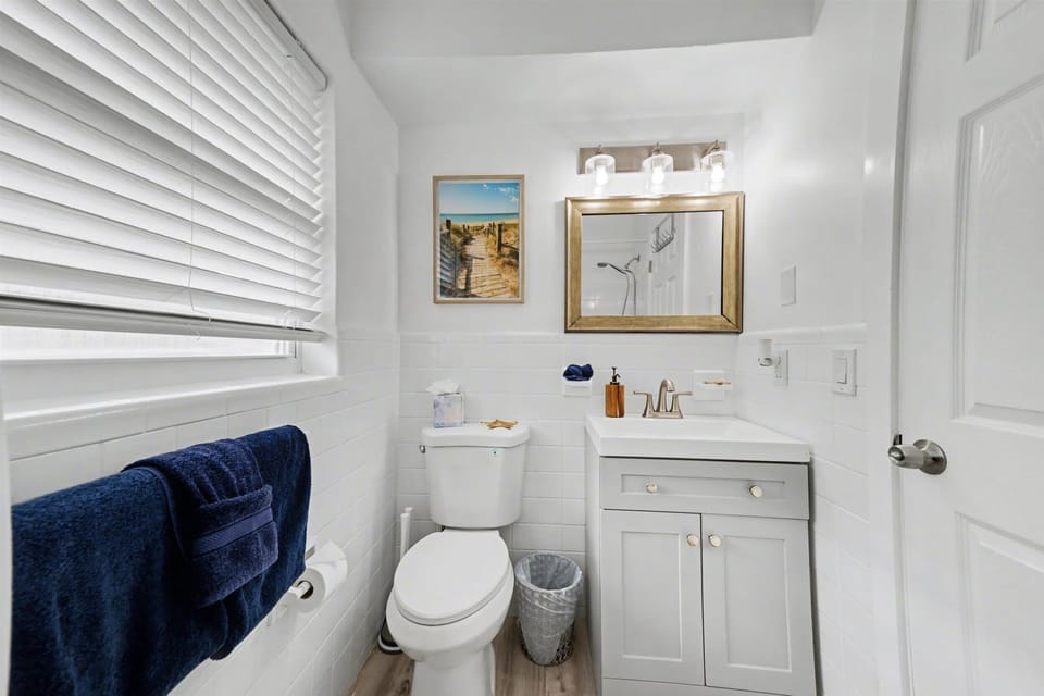Refresh in your coastal-themed bathroom with crisp white finishes, soft natural light from the window, and thoughtful touches like plush navy towels and warm wood accents.