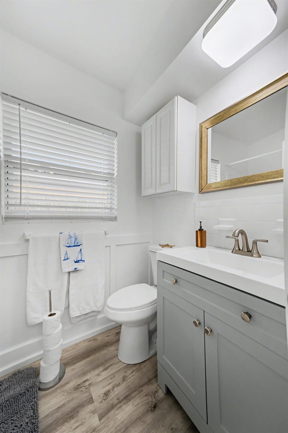 Your bright, coastal-style bathroom combines functionality with charm, featuring warm wood-tone flooring and crisp white finishes that create a fresh, inviting space for your morning routine.