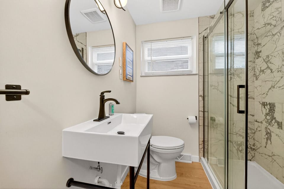 Updated bathroom vanity with round mirror, modern fixtures, and glass shower.