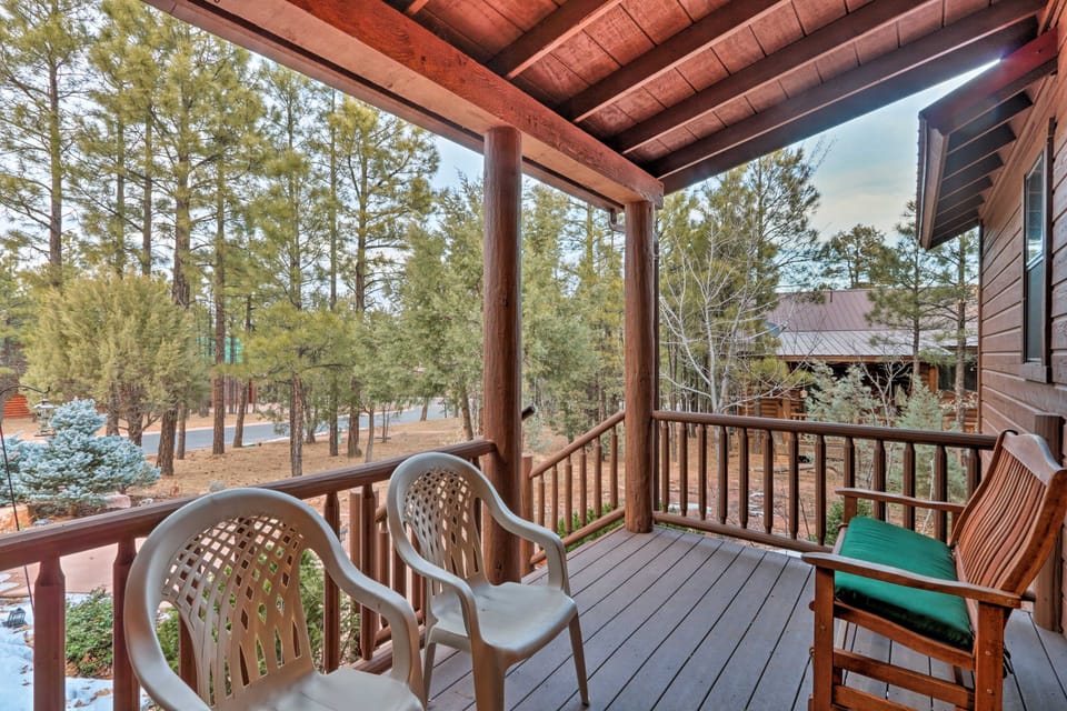 Covered wooden porch with seating overlooking a wooded yard.