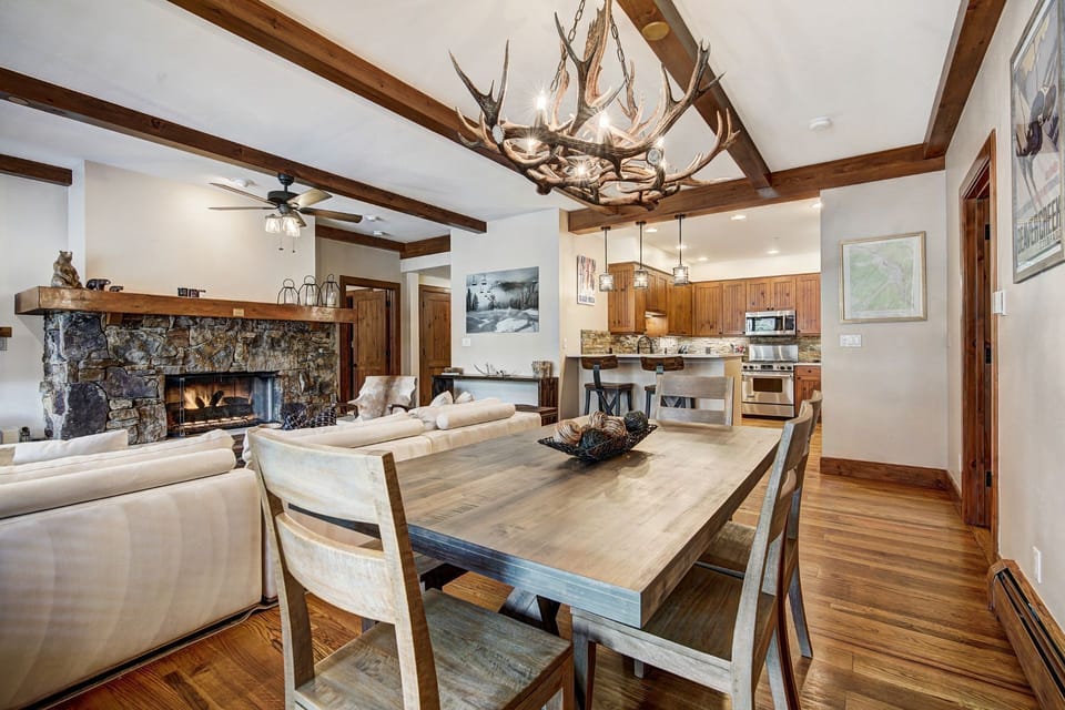 A view of the dining area and living room harmoniously combines rustic elegance, featuring rich wooden accents, a stone fireplace, and inviting seating arrangements.